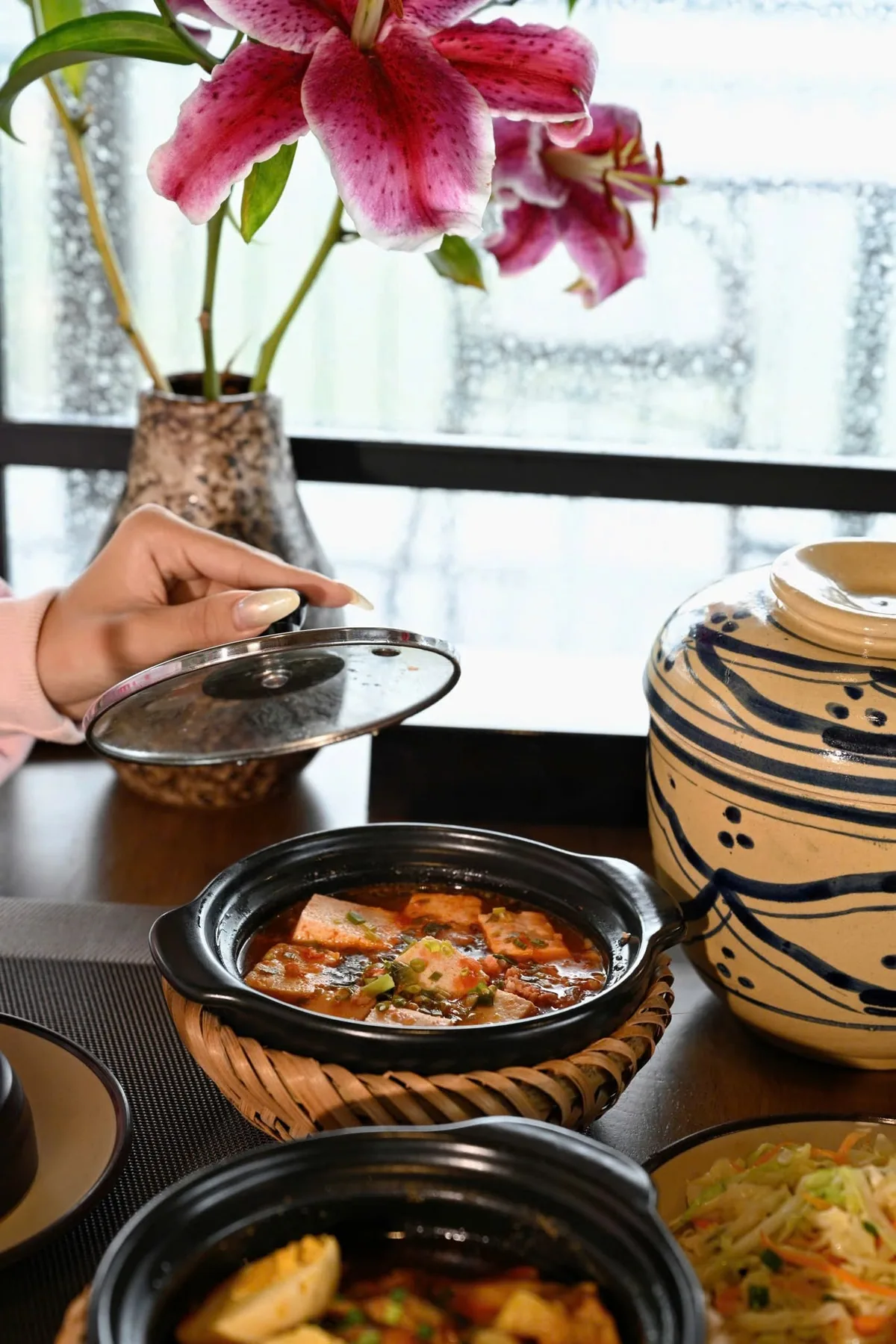 Món ăn trong nồi đất cạnh bình hoa ly